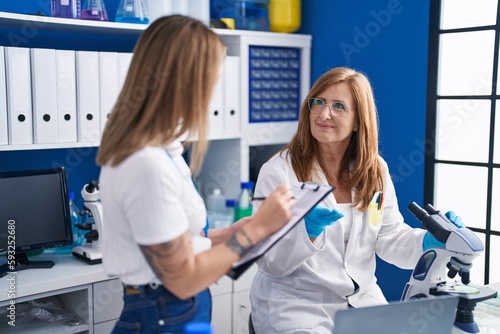 Mother and daughter scientists writing on document using microscope at laboratory