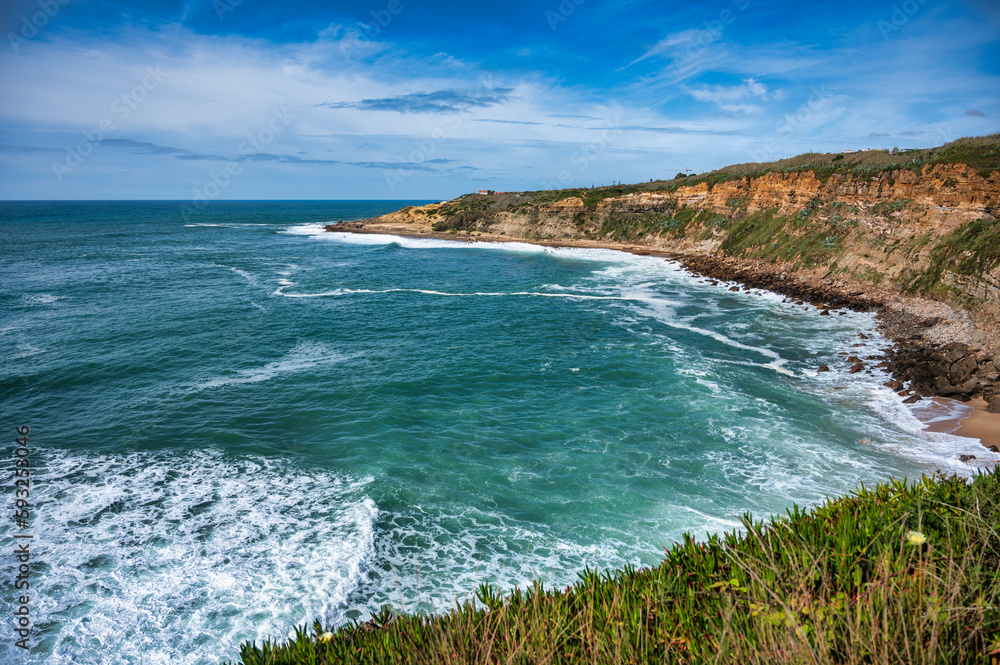 A picturesque view of Coxos bay in Ericeira, Portugal, with dramatic cliffs meeting the powerful, foamy waves of the Atlantic Ocean. A picturesque view of Coxos bay in Ericeira, Portugal, with dramatic cliffs meeting the powerful, foamy waves of the Atlantic Ocean.
