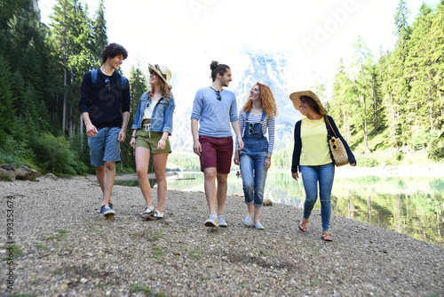 Group of friends of different nationalities on vacation in the middle of nature, walks on the river of an alpine lake and celebrate spring or summer