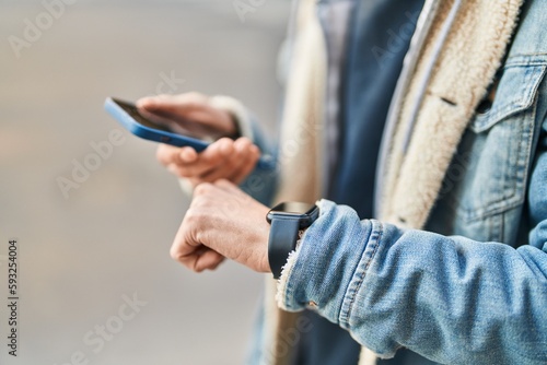 Young hispanic man using smartphone and watch at street