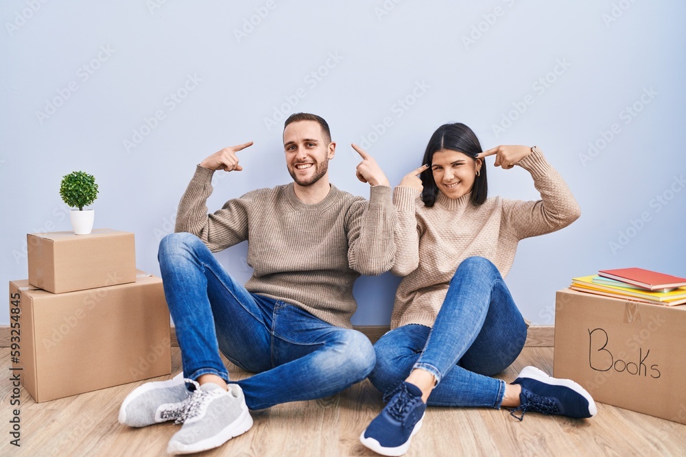 Young couple moving to a new home smiling pointing to head with both hands finger, great idea or thought, good memory Young couple moving to a new home smiling pointing to head with both hands finger, great idea or thought, good memory
