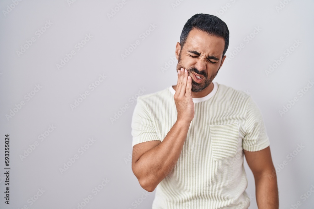Hispanic man with beard standing over isolated background touching mouth with hand with painful expression because of toothache or dental illness on teeth. dentist Hispanic man with beard standing over isolated background touching mouth with hand with painful expression because of toothache or dental illness on teeth. dentist
