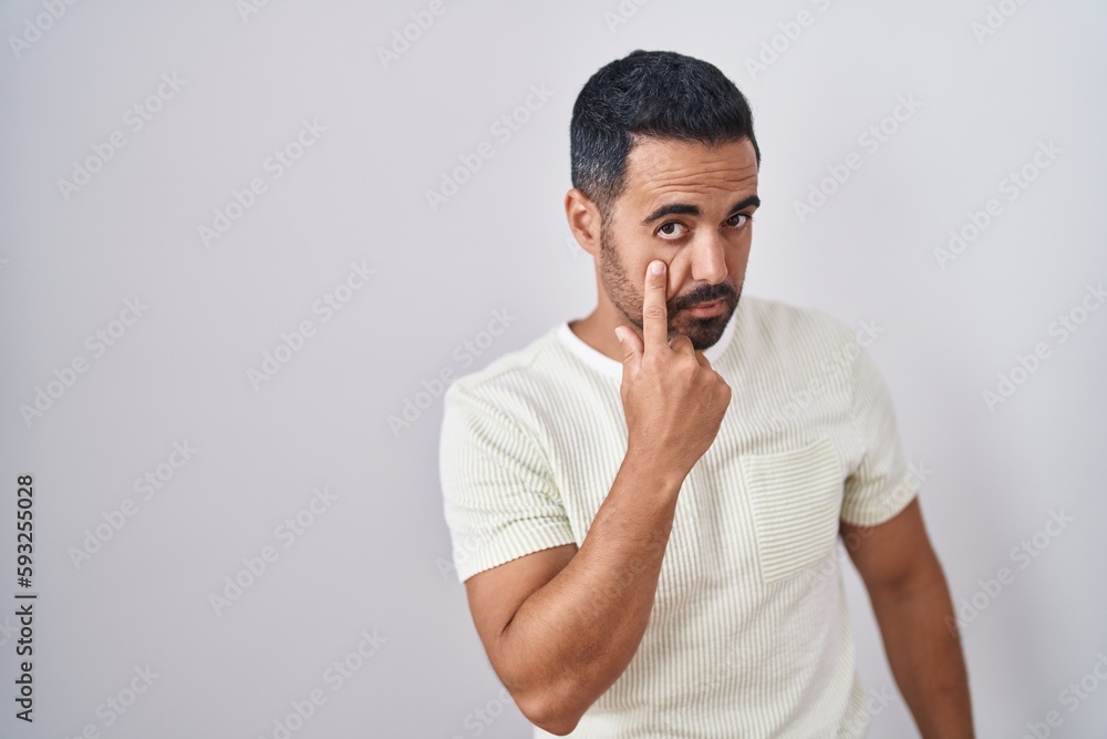 Hispanic man with beard standing over isolated background pointing to the eye watching you gesture, suspicious expression Hispanic man with beard standing over isolated background pointing to the eye watching you gesture, suspicious expression