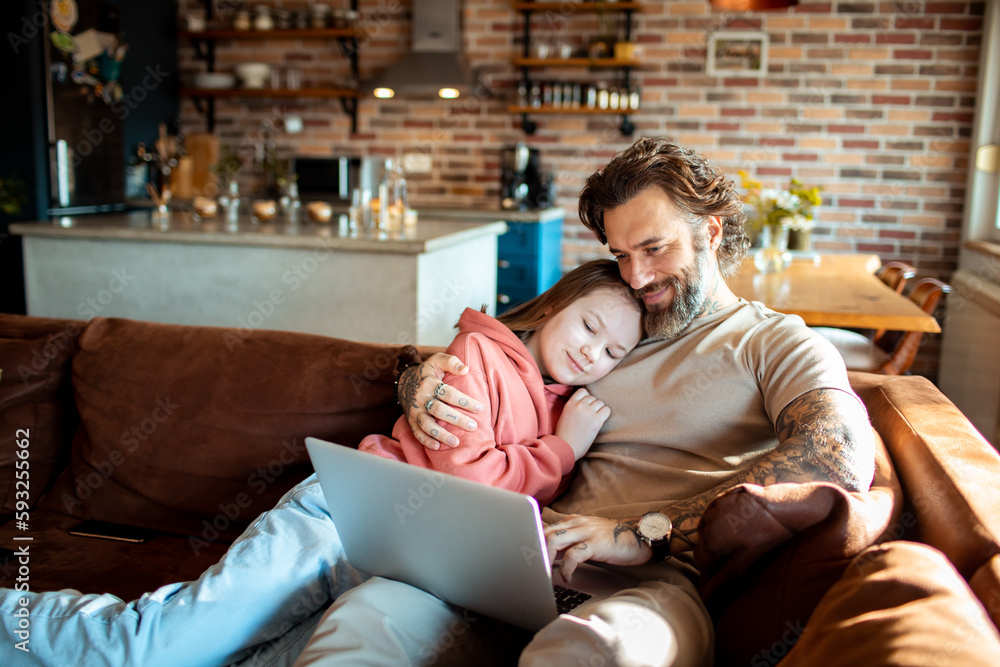 Obraz premium Father and daughter using a laptop on a couch in a living room