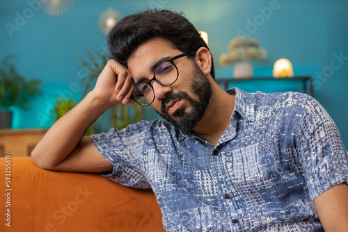 Sad lonely man sitting at home room looks pensive thinks over life concerns or unrequited love suffers from unfair situation. Hindu alone guy problem, break up, depressed feeling bad annoyed burnout