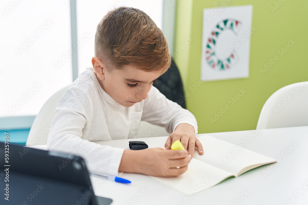 Adorable hispanic boy student using touchpad underlining on notebook at classroom Adorable hispanic boy student using touchpad underlining on notebook at classroom