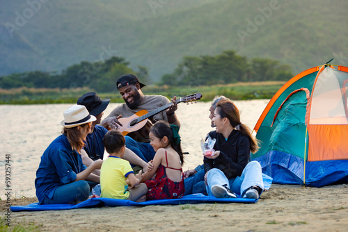 Group of diversity friend and family with kids enjoy playing music together by the camp at the beach and laughing with happiness for leisure summer vacation trip and outdoor travel concept