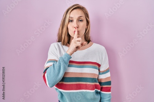 Young blonde woman standing over pink background asking to be quiet with finger on lips. silence and secret concept. © Krakenimages.com