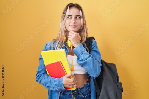 Young blonde woman wearing student backpack and holding books with hand on chin thinking about question, pensive expression. smiling and thoughtful face. doubt concept.
