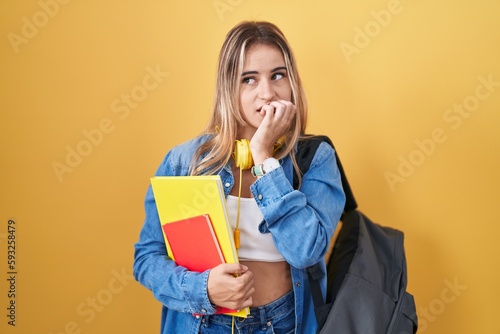 Young blonde woman wearing student backpack and holding books looking stressed and nervous with hands on mouth biting nails. anxiety problem.