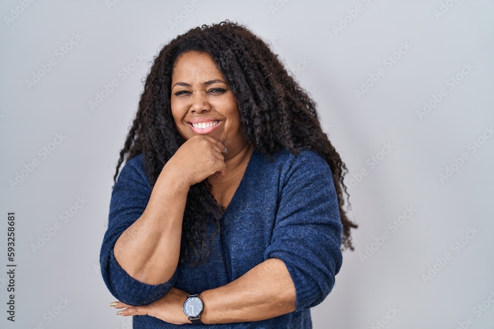 Plus size hispanic woman standing over white background looking confident at the camera smiling with crossed arms and hand raised on chin. thinking positive. Plus size hispanic woman standing over white background looking confident at the camera smiling with crossed arms and hand raised on chin. thinking positive.