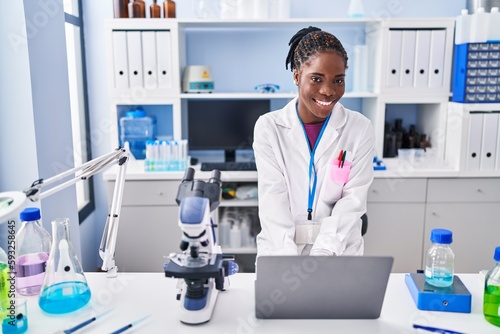 African american woman wearing scientist uniform using laptop at laboratory