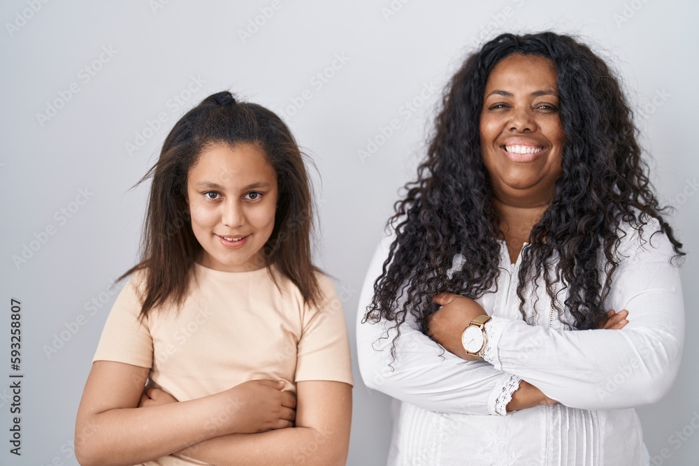 Mother and young daughter standing over white background happy face smiling with crossed arms looking at the camera. positive person. Mother and young daughter standing over white background happy face smiling with crossed arms looking at the camera. positive person.