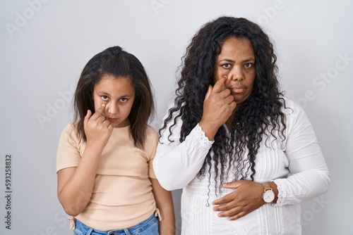 Mother and young daughter standing over white background pointing to the eye watching you gesture  suspicious expression