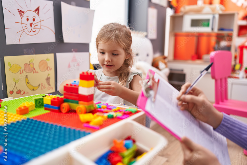 Fototapeta premium Adorable blonde girl playing with construction blocks having therapy at kindergarten