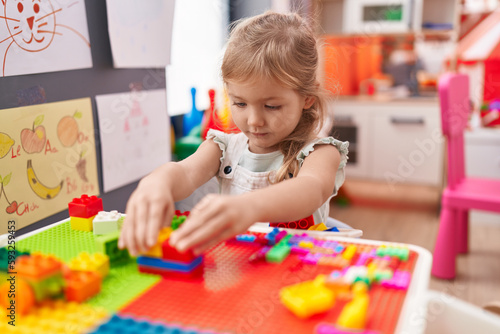 Adorable blonde girl playing with construction blocks sitting on table at kindergarten