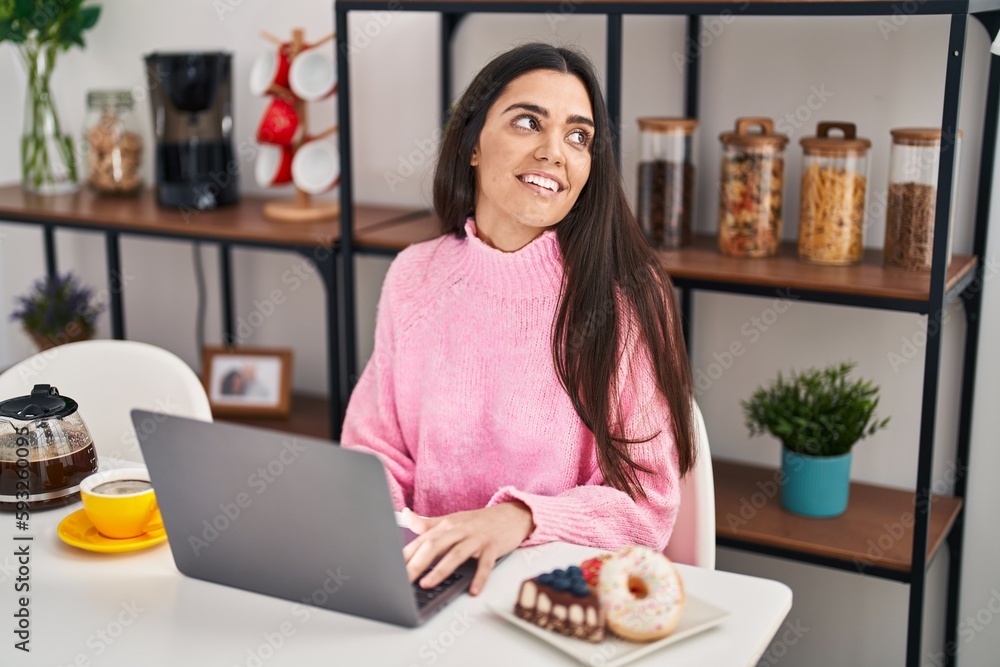 Young hispanic woman using laptop having breakfast at home