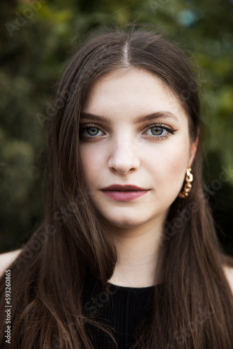 Closeup portrait of a beautiful girl with green eyes and make-up, looking at camera, isolated tree background.