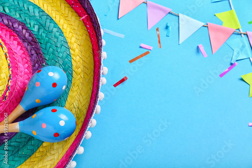 Mexican maracas with sombrero hat, paper flags and confetti on blue background, closeup