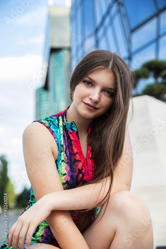 Front portrait of a beautiful female model with long hair and makeup posing behind modern building.