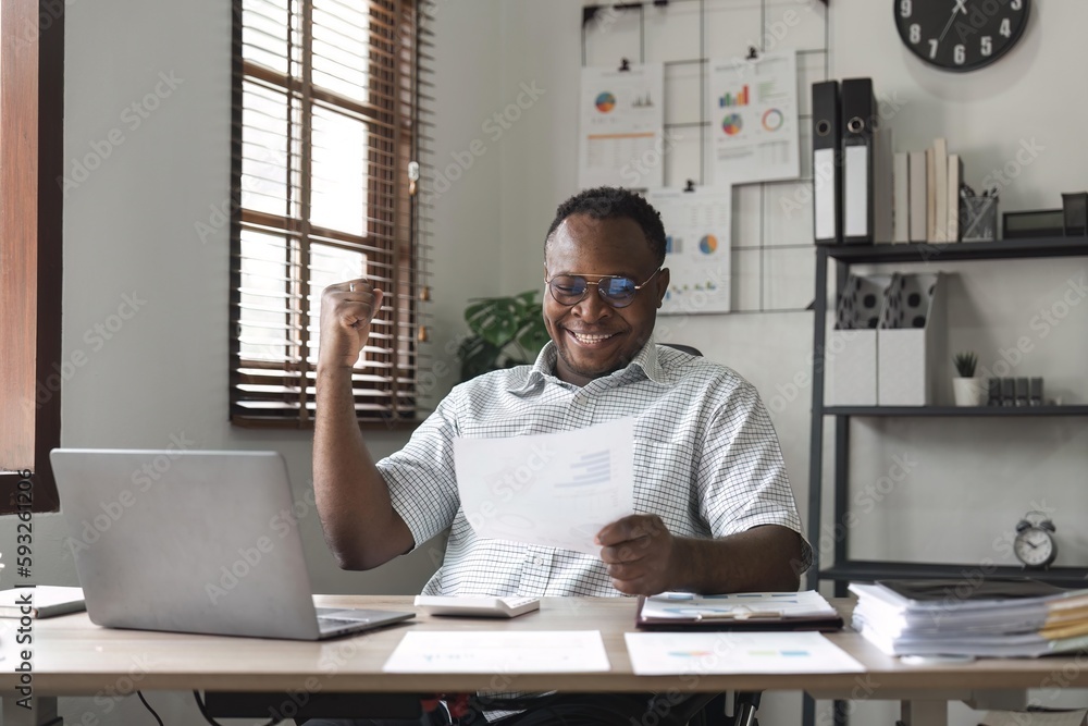 Happy surprised African American businessman reading good news in letter, celebrating success, excited young man holding documents, sitting at work desk Happy surprised African American businessman reading good news in letter, celebrating success, excited young man holding documents, sitting at work desk