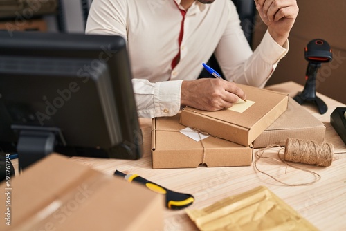 Young hispanic man e-commerce business worker write on package at office