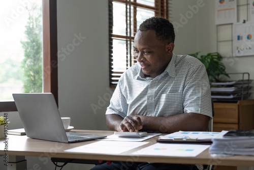 African American man calculating using machine managing household finances at home, focused biracial male make calculations on calculator account taxes or expenses © Natee Meepian