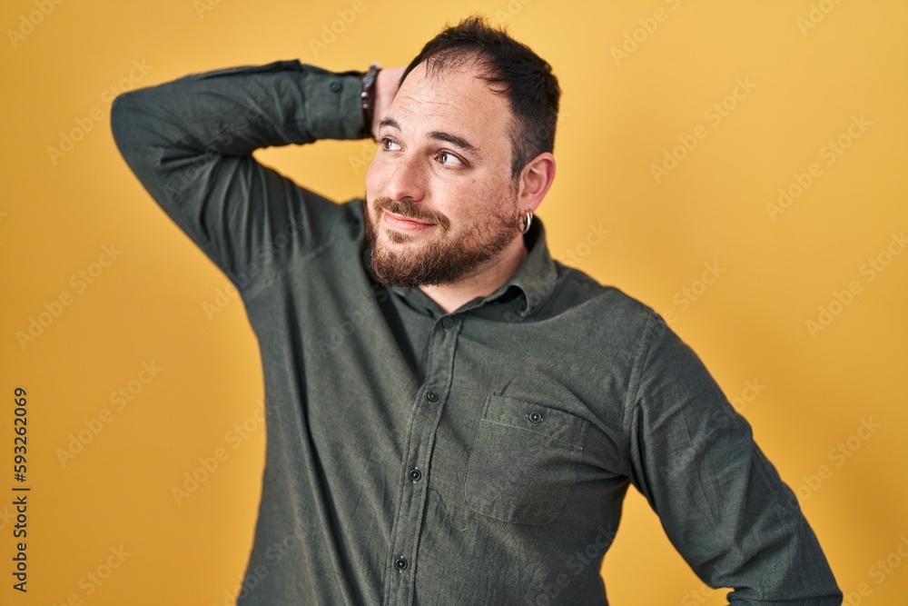 Plus size hispanic man with beard standing over yellow background smiling confident touching hair with hand up gesture, posing attractive and fashionable Plus size hispanic man with beard standing over yellow background smiling confident touching hair with hand up gesture, posing attractive and fashionable