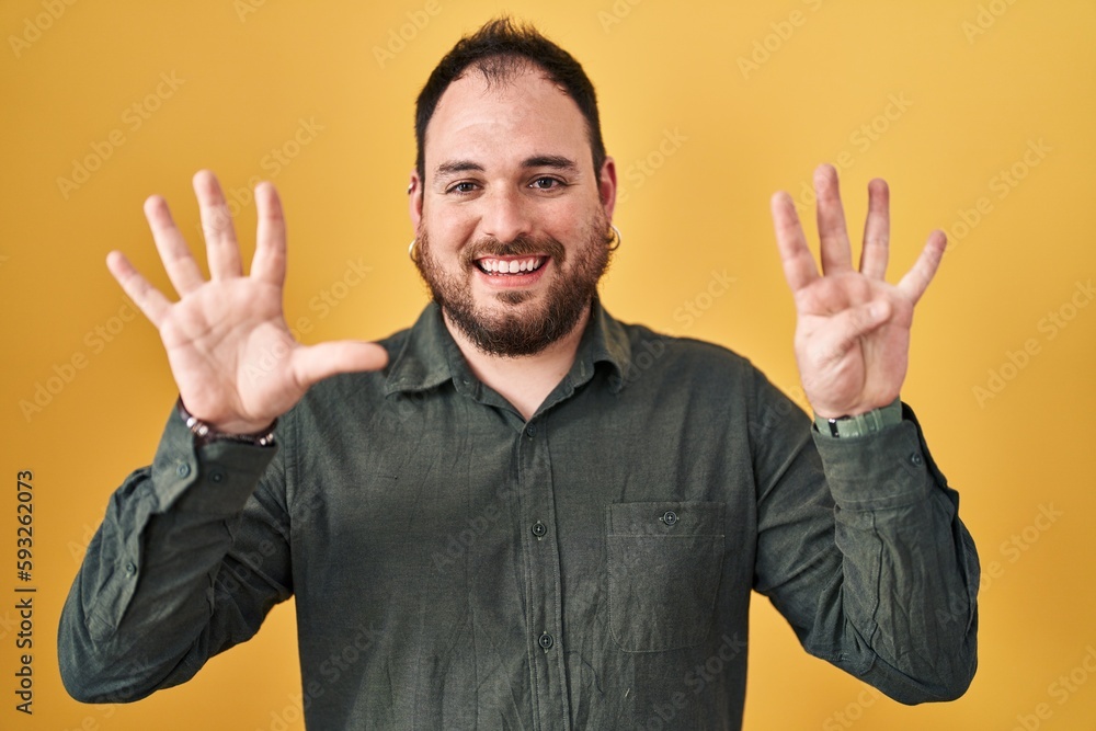 Plus size hispanic man with beard standing over yellow background showing and pointing up with fingers number nine while smiling confident and happy. Plus size hispanic man with beard standing over yellow background showing and pointing up with fingers number nine while smiling confident and happy.