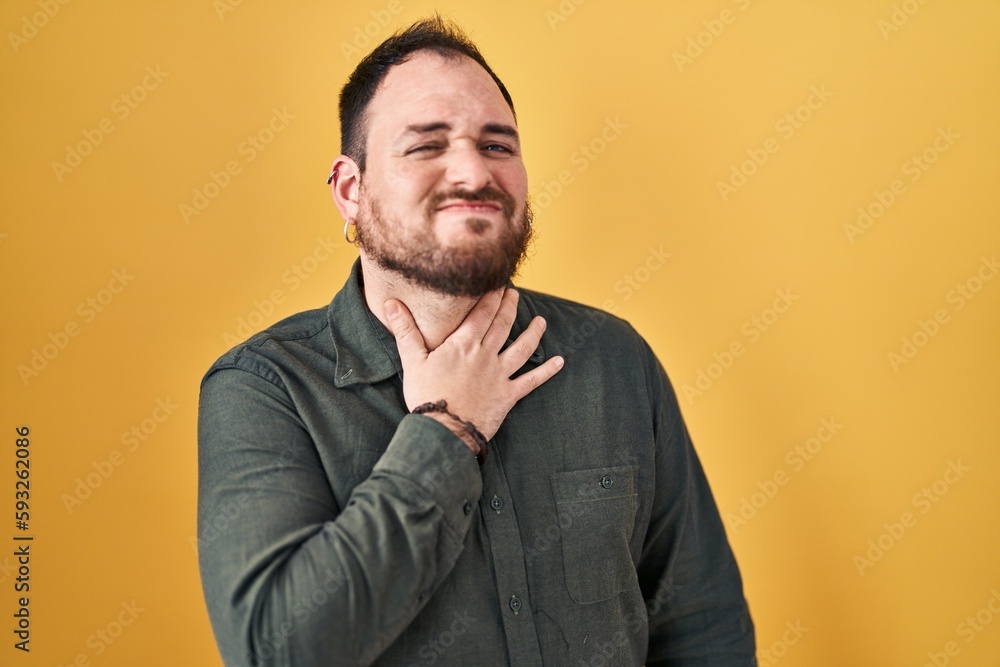 Plus size hispanic man with beard standing over yellow background touching painful neck, sore throat for flu, clod and infection Plus size hispanic man with beard standing over yellow background touching painful neck, sore throat for flu, clod and infection