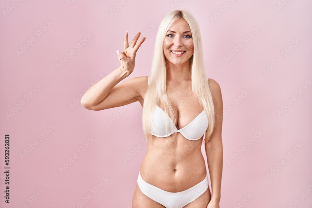 Obraz premium Caucasian woman wearing lingerie over pink background showing and pointing up with fingers number three while smiling confident and happy.