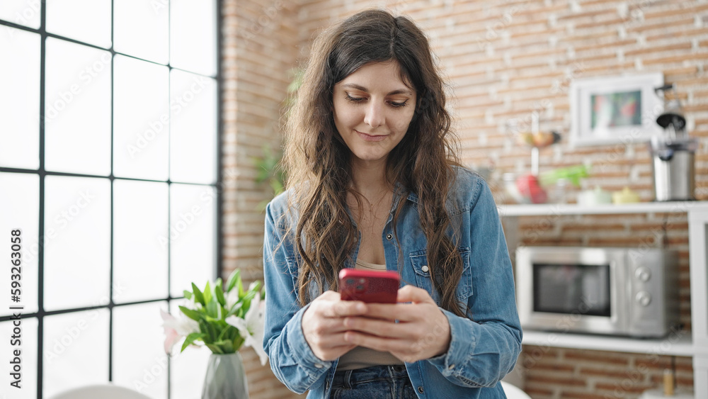 Young beautiful hispanic woman using smartphone sitting on table at dinning room Young beautiful hispanic woman using smartphone sitting on table at dinning room