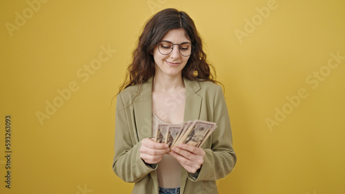 Young beautiful hispanic woman smiling confident counting dollars over isolated yellow background