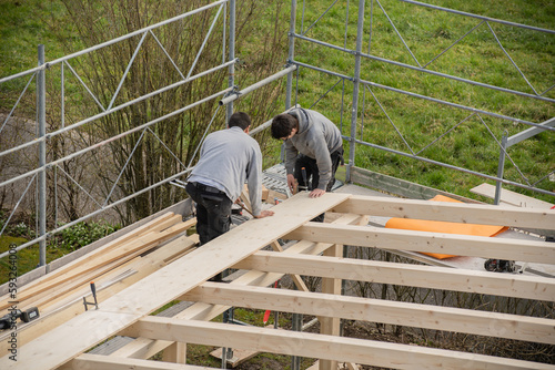 Two young carpenters building a carport. Apprentice learns from trainer.