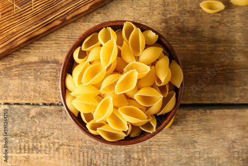 Bowl with raw conchiglie pasta on wooden background photo