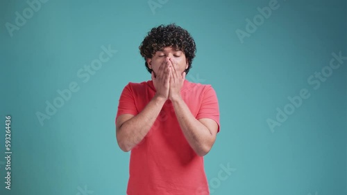 young Indian handsome man looking happy and excited, shocked with an unexpected surprise with both hands open next to face on blue studio background