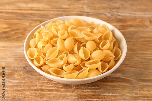 Bowl with raw conchiglie pasta on wooden background photo