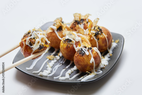 Takoyaki (octopus balls) on a plate isolated, one of the balls is picked up by chopsticks, isolated white background