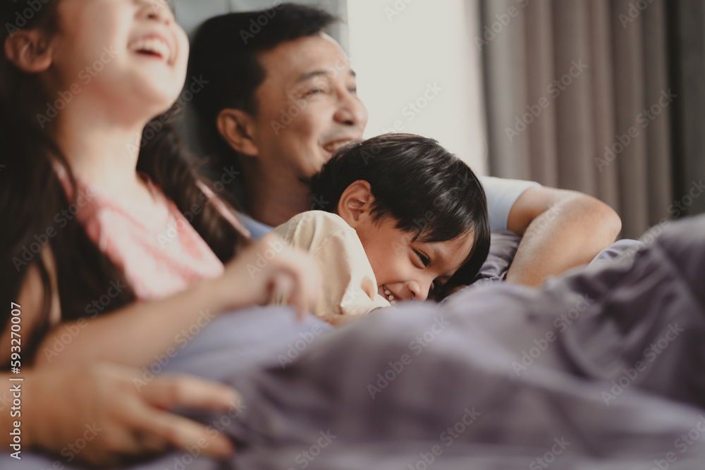 Handsome young Asian father embracing and hugging cute little Asian boy and son while preparing for for a good night sleep at home on a comfortable bed Handsome young Asian father embracing and hugging cute little Asian boy and son while preparing for for a good night sleep at home on a comfortable bed