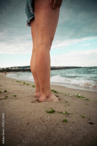 Barefoot female standing on wet sandy beach by the sea, vertical shot