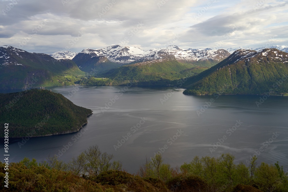 Aerial view of a fjord in Sjoholt, Norway surrounded by green mountains with snowy peaks in summer