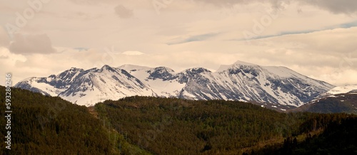 Panoramic view of a snowy mountain range near Sjoholt, Norway against green hills on a cloudy day photo