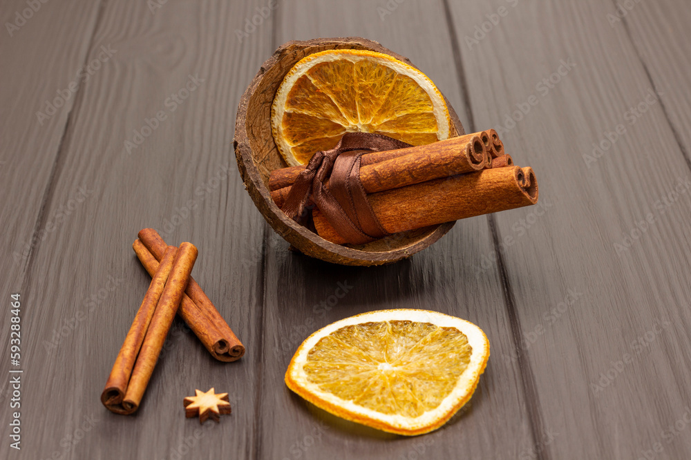 Cinnamon sticks tied in a bunch and orange chips in a coconut shell. Cinnamon sticks on the table.