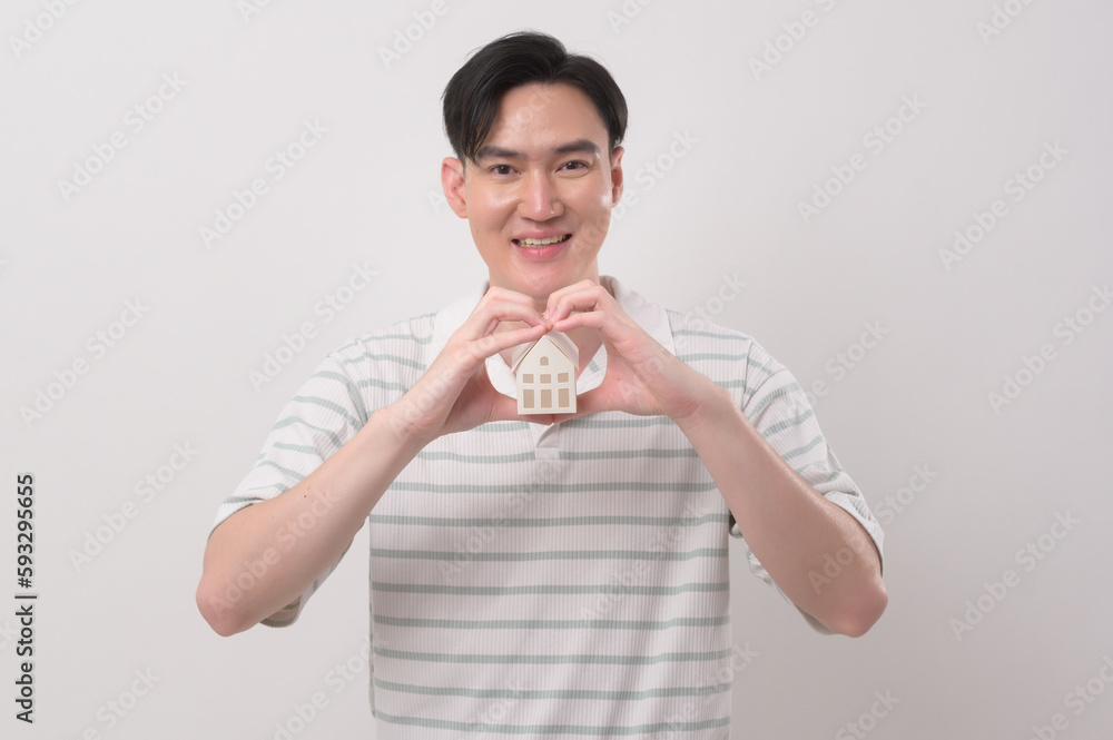 Young smiling man holding small model house over white background studio.. Young smiling man holding small model house over white background studio..
