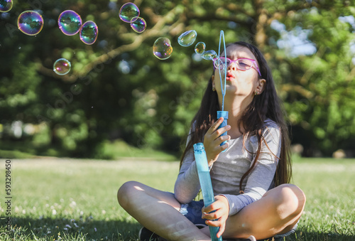 Portrait of a beautiful caucasian girl blows soap bubbles  sits cross-legged in a flower meadow