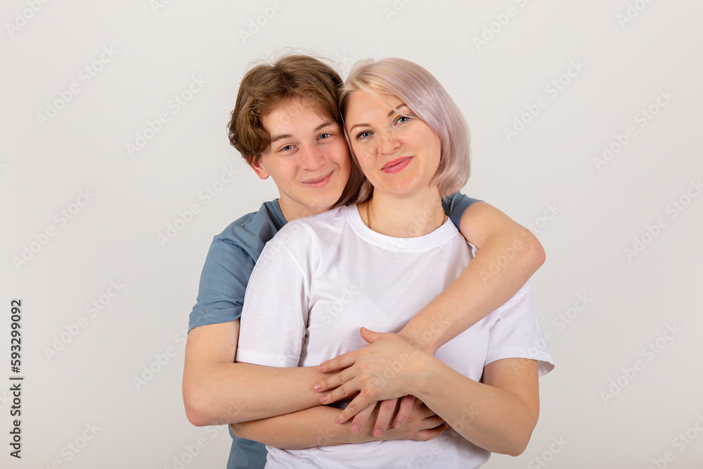 Mothers day, children and family concept - teen boy hugging his mom on white background Mothers day, children and family concept - teen boy hugging his mom on white background