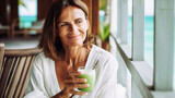 Middle aged caucasian woman with brown hair enjoying a healthy green smoothie on a tropical hotel terrace, AI Generated