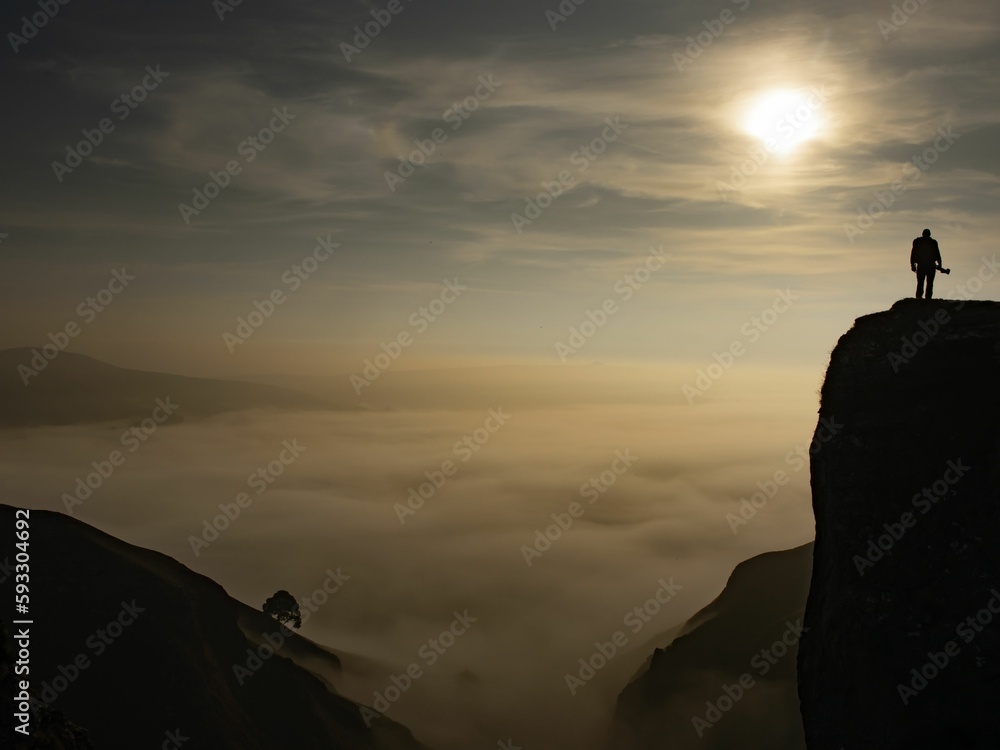 Cloud inversion peak with tree and man in silhouette during sunset