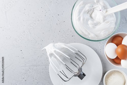 Whipped egg whites - whipped Italian meringue on a wire whisk, eggs, sugar, on a gray background. copy space.
