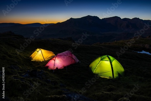 Colorful tents lit up in a lake district at national park with Scafell Pike at nightfall